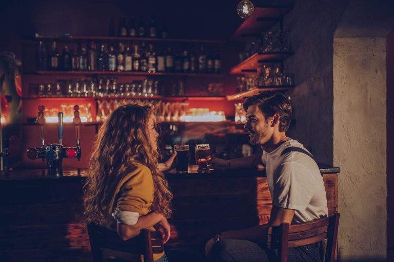 A young couple at a bar looking at each other with a beer in their hands