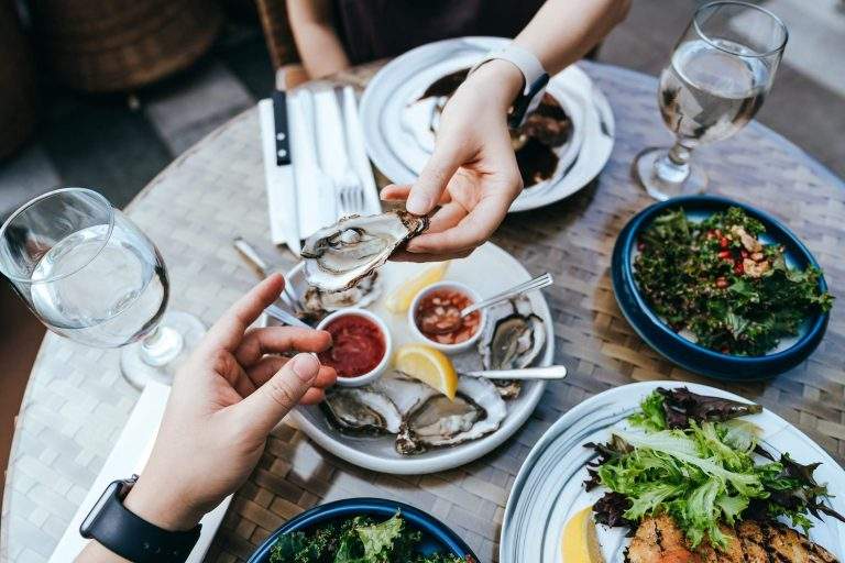 A close-up of a restaurant table with a couple's hands sharing oysters