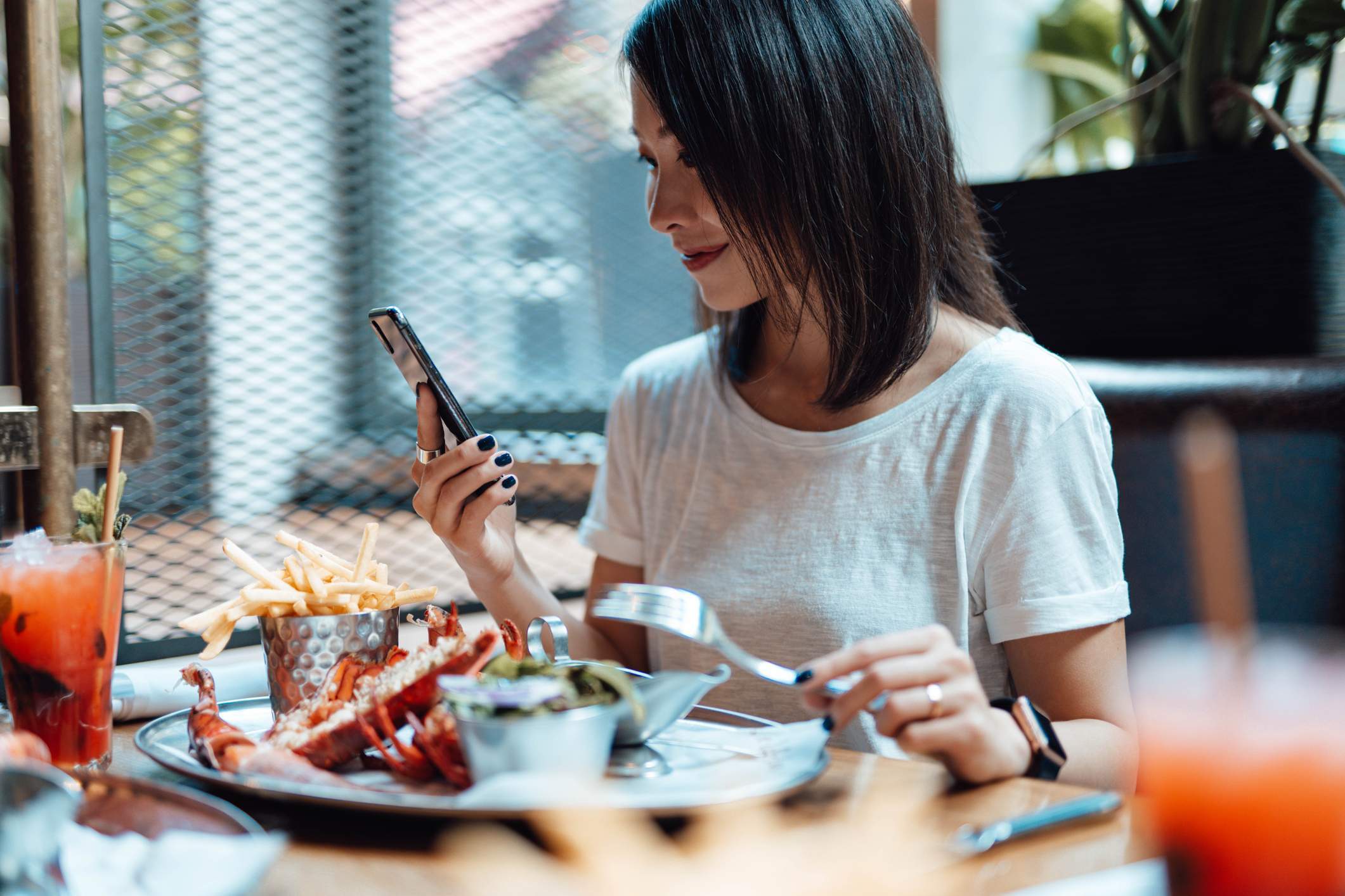 A restaurant customer is enjoying her meal while looking at her mobile phone
