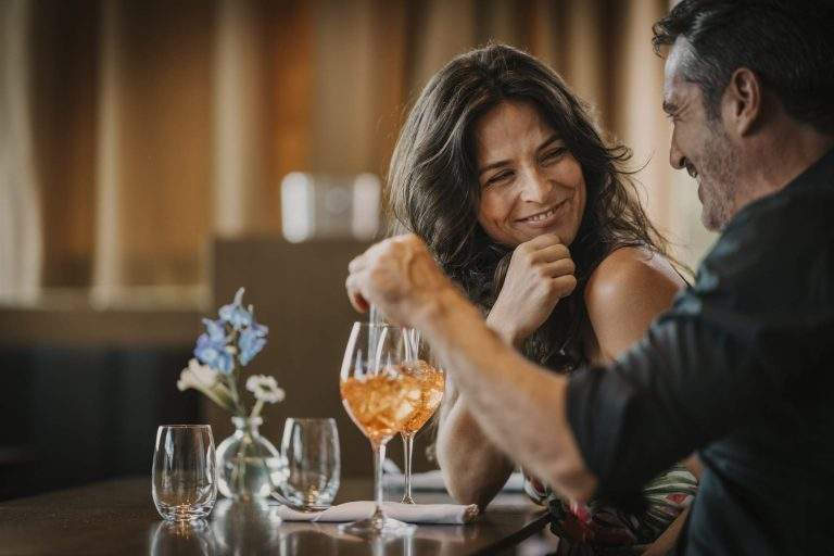 A man and a woman drinking a cocktail at a restaurant and looking at each other smiling
