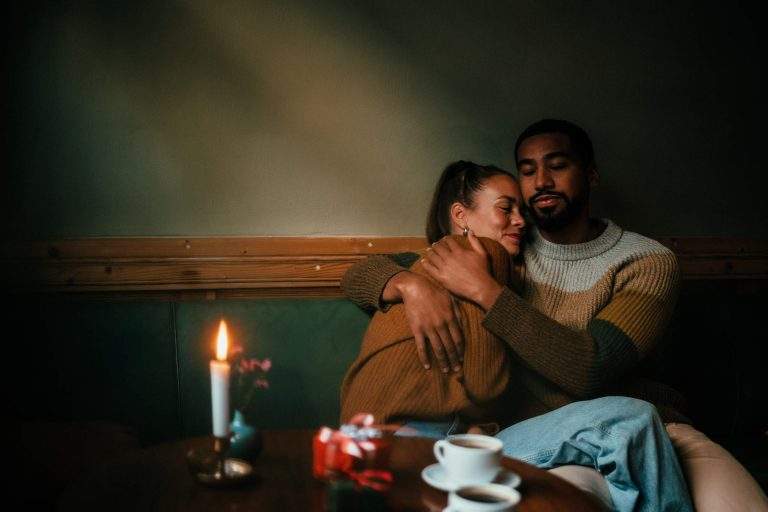 A couple at a restaurant hugging each other in front of a dining table with a candle and two coffees