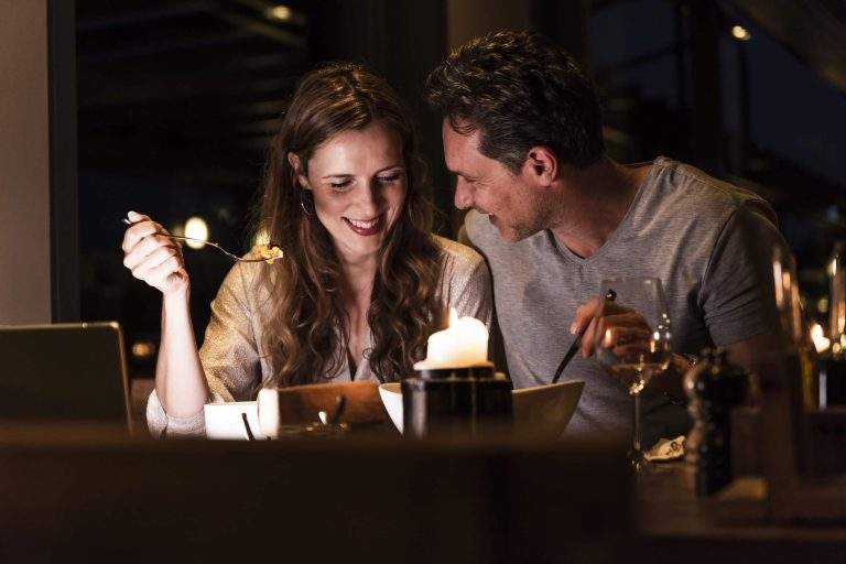 A couple smiling at each other and eating at a restaurant
