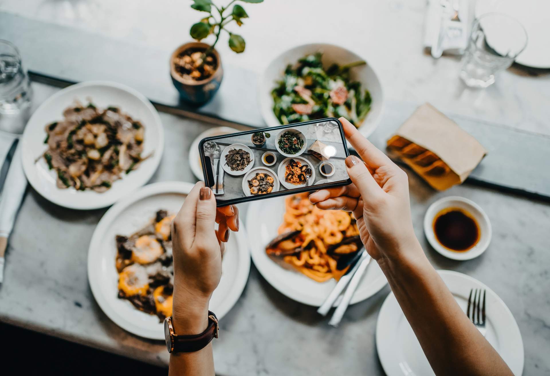 A social media influencer is taking a picture of dishes they've ordered in a restaurant