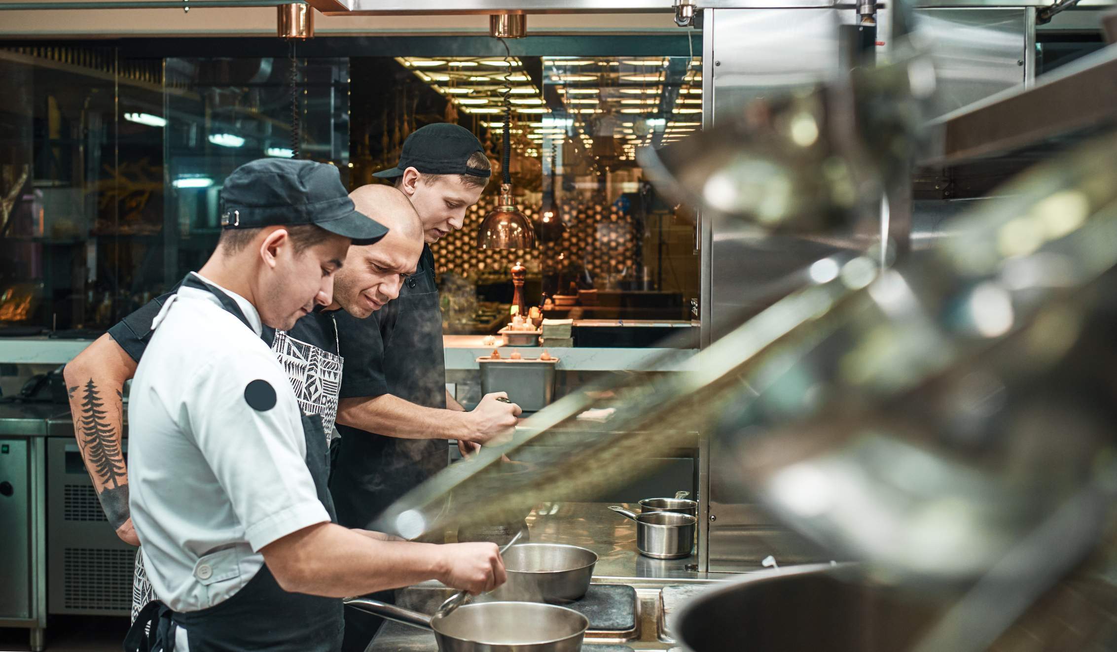 This image shows a restaurant kitchen setting where 3 restaurant staff are working behind the scene